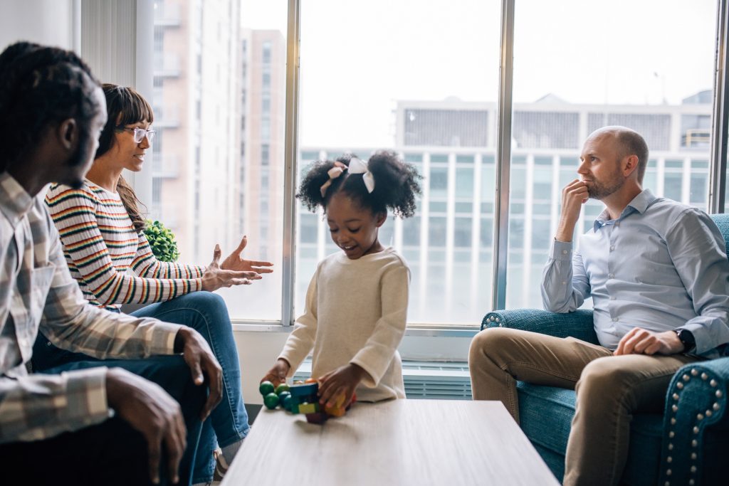 little girl playing while parents tale to Doctor